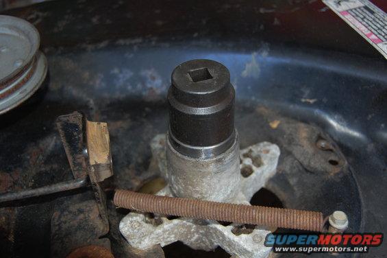 Close-up of a rusty lawn mower deck spindle with a socket wrench on top and a spring below