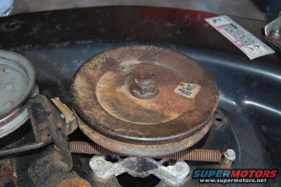 Close-up of a rusty pulley on a lawn mower deck with a spring and tensioner visible