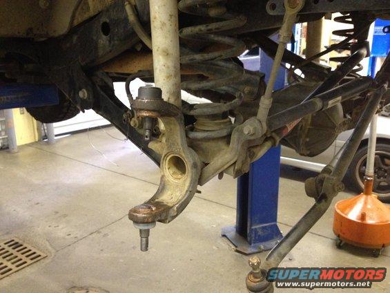 Close-up of a vehicle's front suspension, showing a ball joint assembly removed from the knuckle