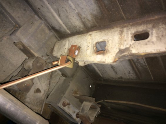 Underbody view of a broken fuel tank strap and rusted frame
