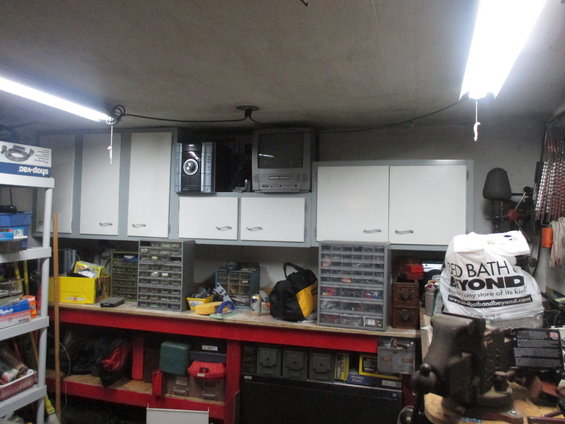 Garage workbench with white cabinets, storage drawers, a vise, and a shopping bag