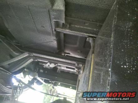 Underside of a dark-colored vehicle, showing frame and suspension components. Watermark reads SUPERMOTORS.NET