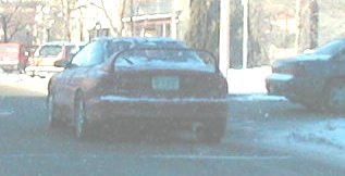 red sports car with large rear spoiler and aftermarket exhaust tip, parked on snowy street