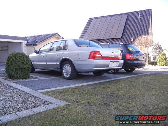 silver sedan parked next to a dark SUV in a driveway, house with solar panels in background