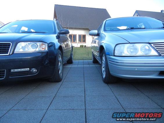 black Audi and a light blue car parked on a paved driveway in front of a house