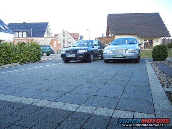 Silver sedan front view parked in driveway next to a dark sedan