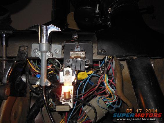 Dashboard wiring harness with exposed wires and a lit bulb