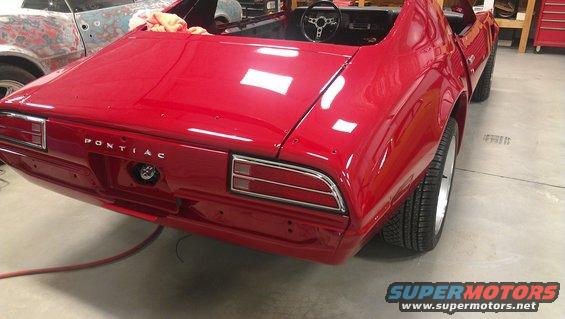 Red Pontiac Firebird undergoing restoration, rear view, showing "PONTIAC" badging and taillights
