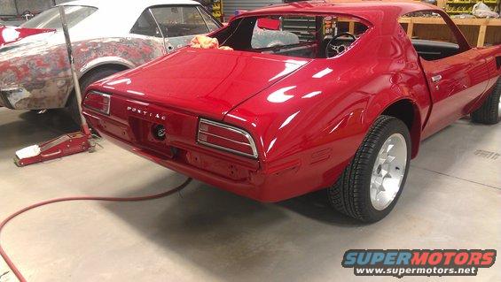 Rear view of a red 1970 Pontiac Firebird in a garage, with another car in primer behind it
