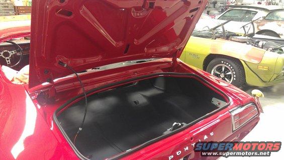 Red car's open trunk and interior, with a yellow car in the background. The red car has 'PONTIAC' visible on the trunk lid