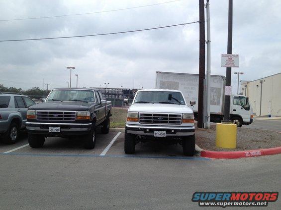 Two 1997 Ford F-350 trucks parked side-by-side, one black and one white, viewed from the front