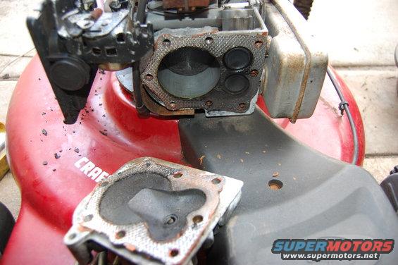 Close-up of a disassembled lawn mower engine, showing the cylinder head and gasket removed. The red deck has 'CRAFTSMAN' visible