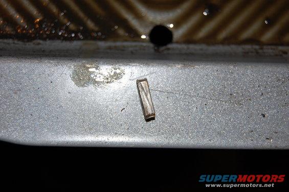 Small metal pin lying on a gray, textured surface with some liquid residue
