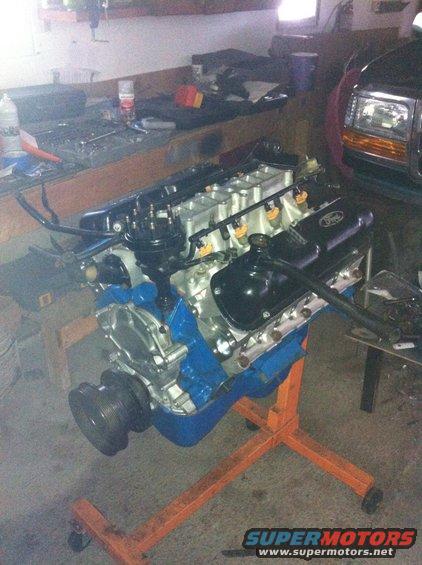 Ford V8 engine on an orange engine stand, with a portion of a dark SUV visible in the background