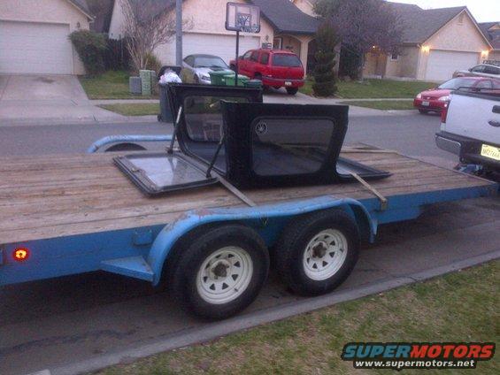 Jeep CJ-series soft top disassembled on a blue trailer, with houses and other vehicles in the background