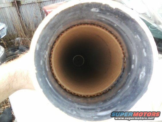 Cardboard tube with black rubbery exterior, viewed from one end into a dark interior. Corrugated cardboard edge visible