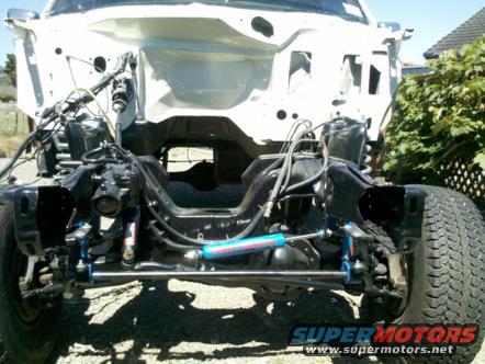 White Ford Bronco chassis with exposed engine bay, blue shock absorbers, and black frame