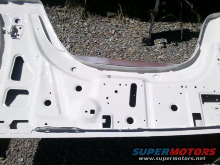 White painted vehicle frame section with numerous holes and cutouts