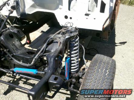 Vehicle frame with suspension, blue shock absorbers, and tire. White body shell visible