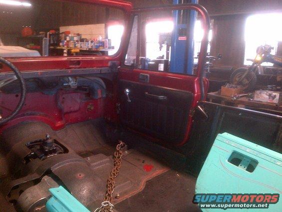 Red Jeep interior with open door, showing floor, steering wheel, and dashboard. A turquoise door lies nearby