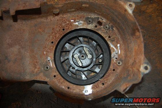 Recoil starter assembly with black plastic housing and metal pull mechanism, mounted on heavily rusted metal