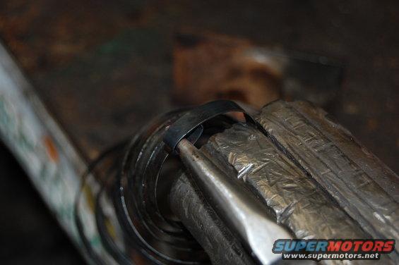 Metal part being held in a vise with a tool working on it. Supermotors.net logo visible