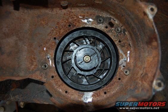 Rusty metal recoil starter housing with a black plastic fan and a gold bolt