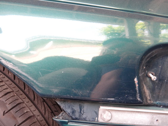 Green car fender with scratches and a dent near the wheel well, showing a tire and part of a black plastic trim piece
