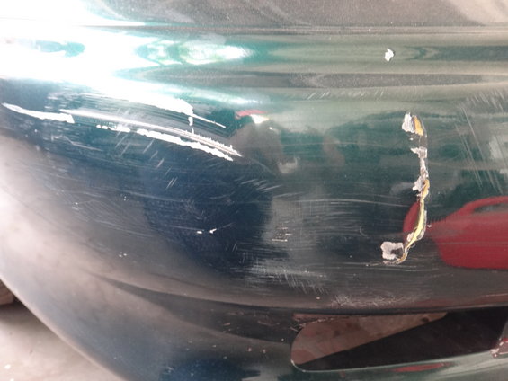 Close-up of a green car bumper with significant scratches and paint damage