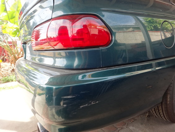Rear bumper and taillight of a dark green car. Bumper has many scratches