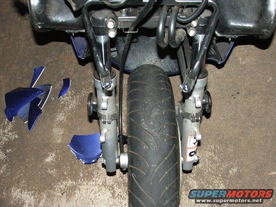 Front wheel and suspension of a motorcycle with broken blue body panels scattered nearby
