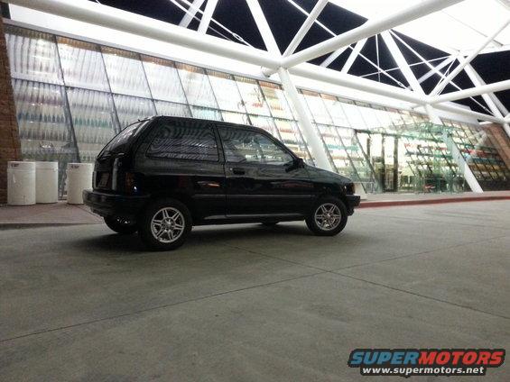 Black 1991 Ford Festiva parked outside a modern building with a glass facade