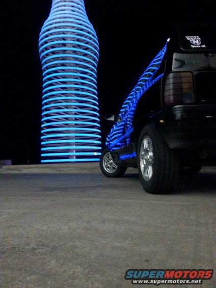 Black car with blue neon lights near a giant illuminated bottle
