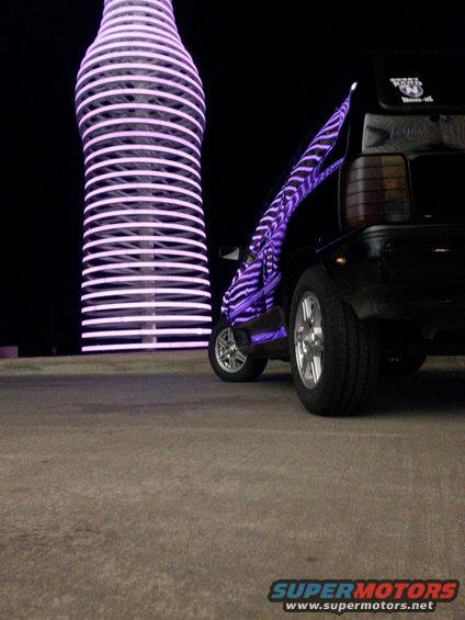 black hatchback with purple zebra stripes parked by giant glowing bottle at night