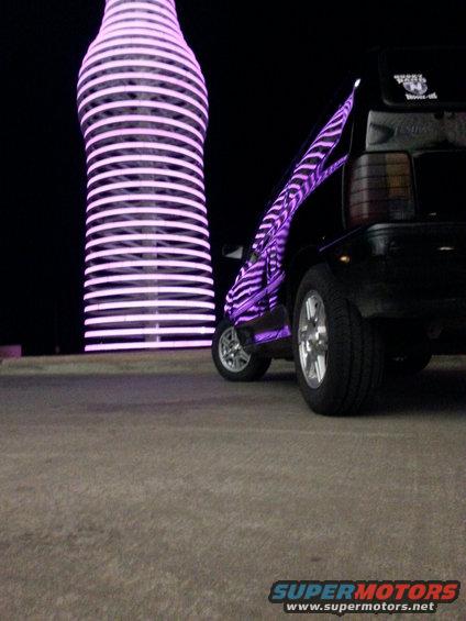 Black car with purple zebra stripes parked next to a giant illuminated bottle sculpture