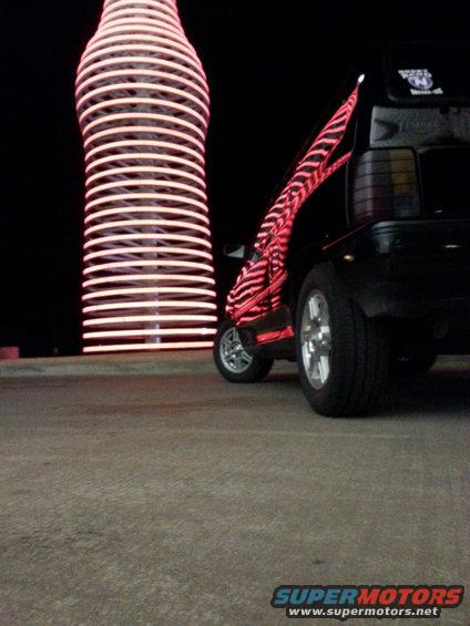 Black car with red zebra stripe decal on rear quarter panel, parked near a tall, illuminated bottle-shaped structure