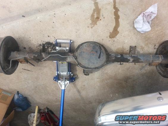 Rear axle assembly supported by a blue floor jack on a concrete floor