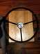 1964 Ford Fairlane - A black steering wheel is shown from above, placed on a wooden surface.