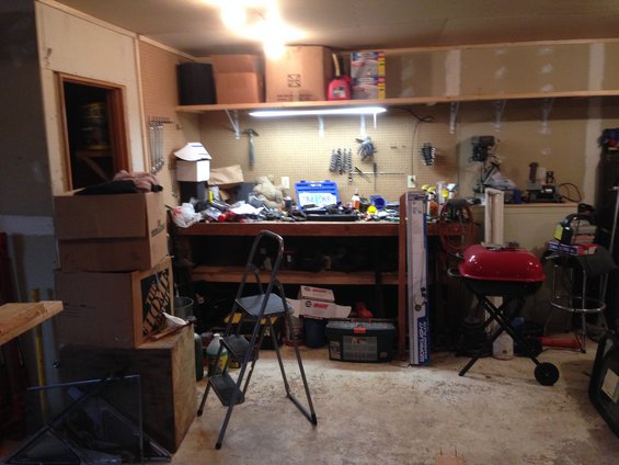 Garage interior with a workbench cluttered with tools and boxes, a red grill, and a step ladder
