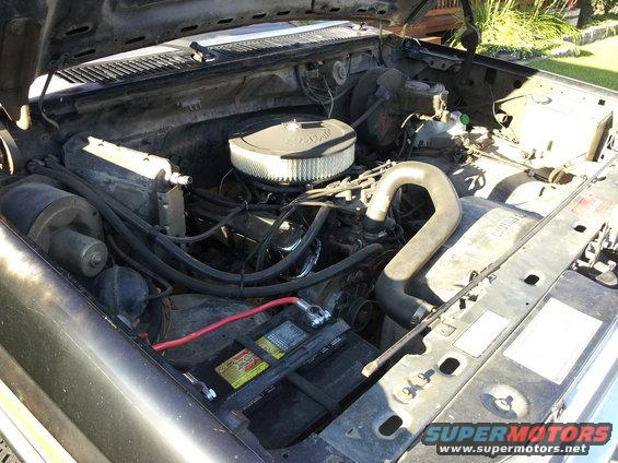 Engine bay with air filter, battery, and hoses visible