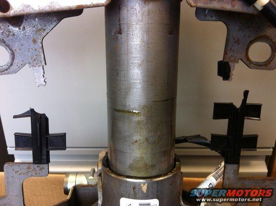 Close-up of a metal steering column with black rubber mounts attached to metal brackets