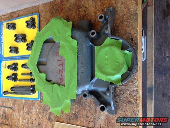 automotive part covered in green masking tape, with two packages of fasteners nearby