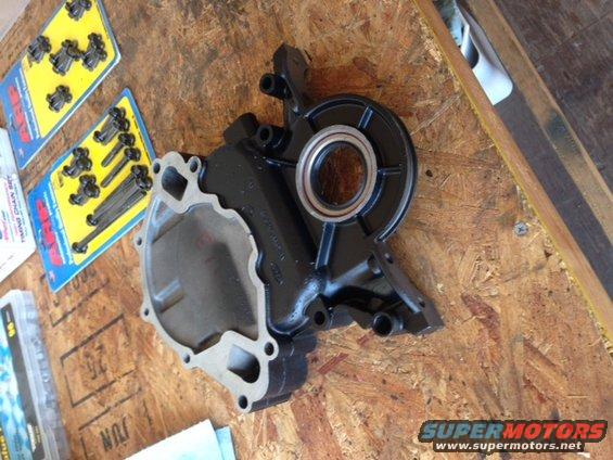 Black engine water pump with bearing, next to packaged bolts on plywood