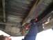 1964 Ford Ranchero - A person works on the underside of a wooden truck bed, hammering a rusted metal support beam.
