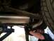 1964 Ford Ranchero - A mechanic works on the exhaust system of a vehicle, with a leaf spring and tire visible.