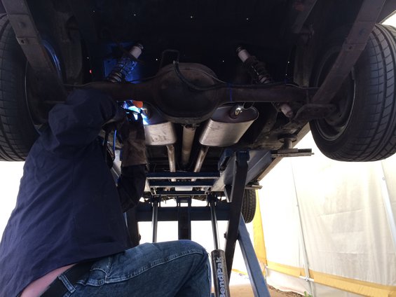 Person welding exhaust pipes under a car lifted on a lift