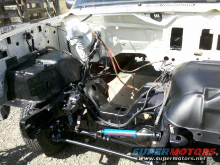 White Ford Bronco engine bay with exposed frame and wiring, blue shock absorber visible