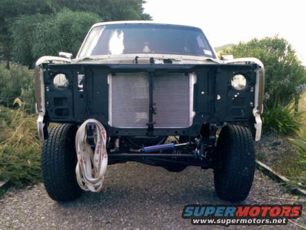 Front of a truck with no grille or fenders, showing the radiator and suspension components. A tow strap hangs from the frame