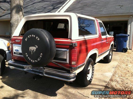 Red and white Ford Bronco with spare tire on rear, parked in driveway