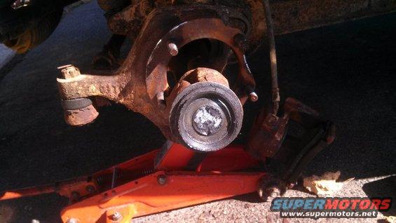 rusted suspension part on orange jack, part of a vehicle's wheel assembly